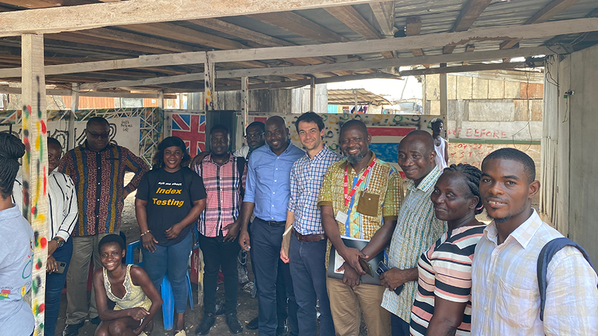 About a dozen people smile for the camera in a rustic structure in Ghana.