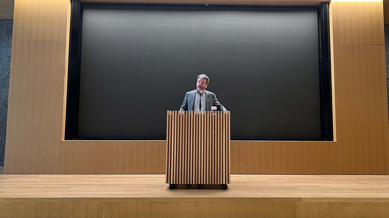 A man speaks at a wooden podium.