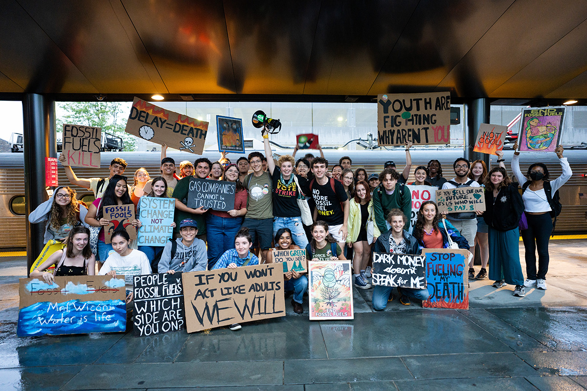 Princeton students holding signs to protest the use of fossil fuels are posed on a train platform