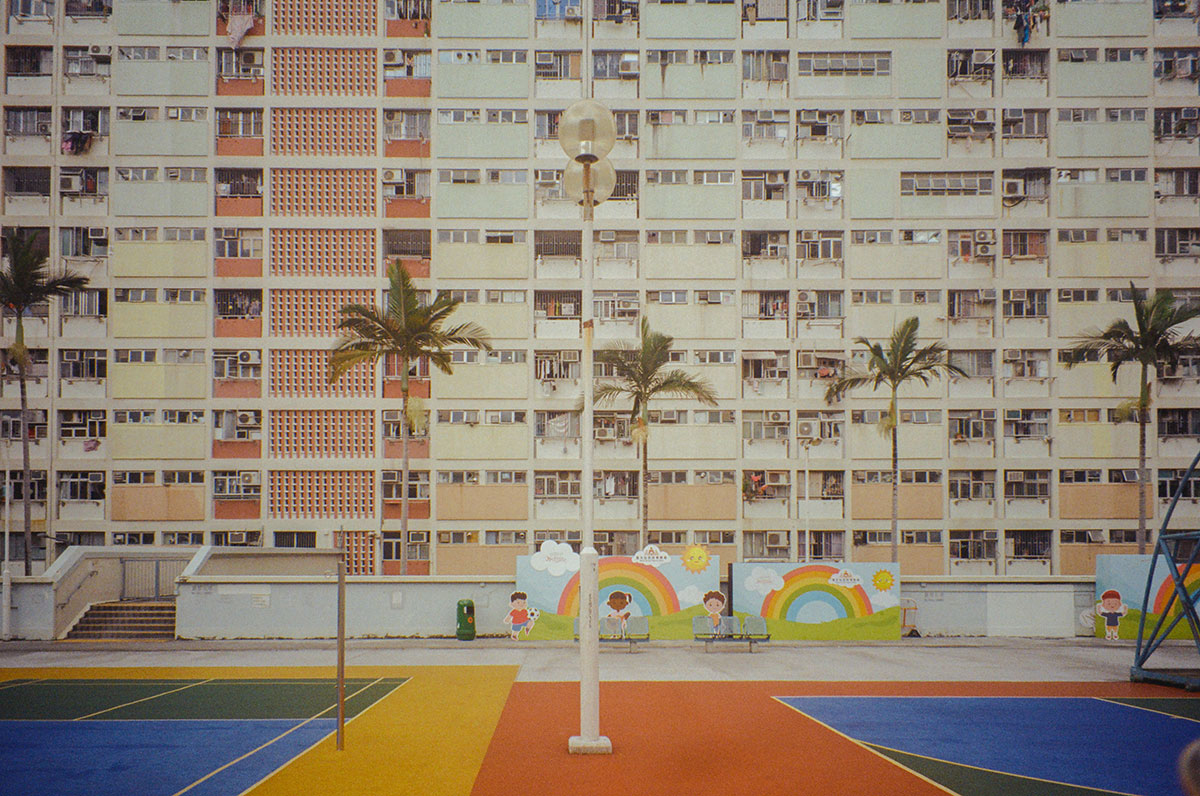 Brightly colored tennis courts are separated by a row of palm trees from two rainbow murals and an apartment building.