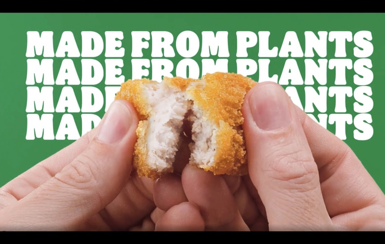 Fingers break open a vegan chicken nugget with the words "Made from plants" in the background.