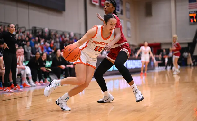 A Princeton basketball player dribbles inside, guarded tightly by a Harvard player. 