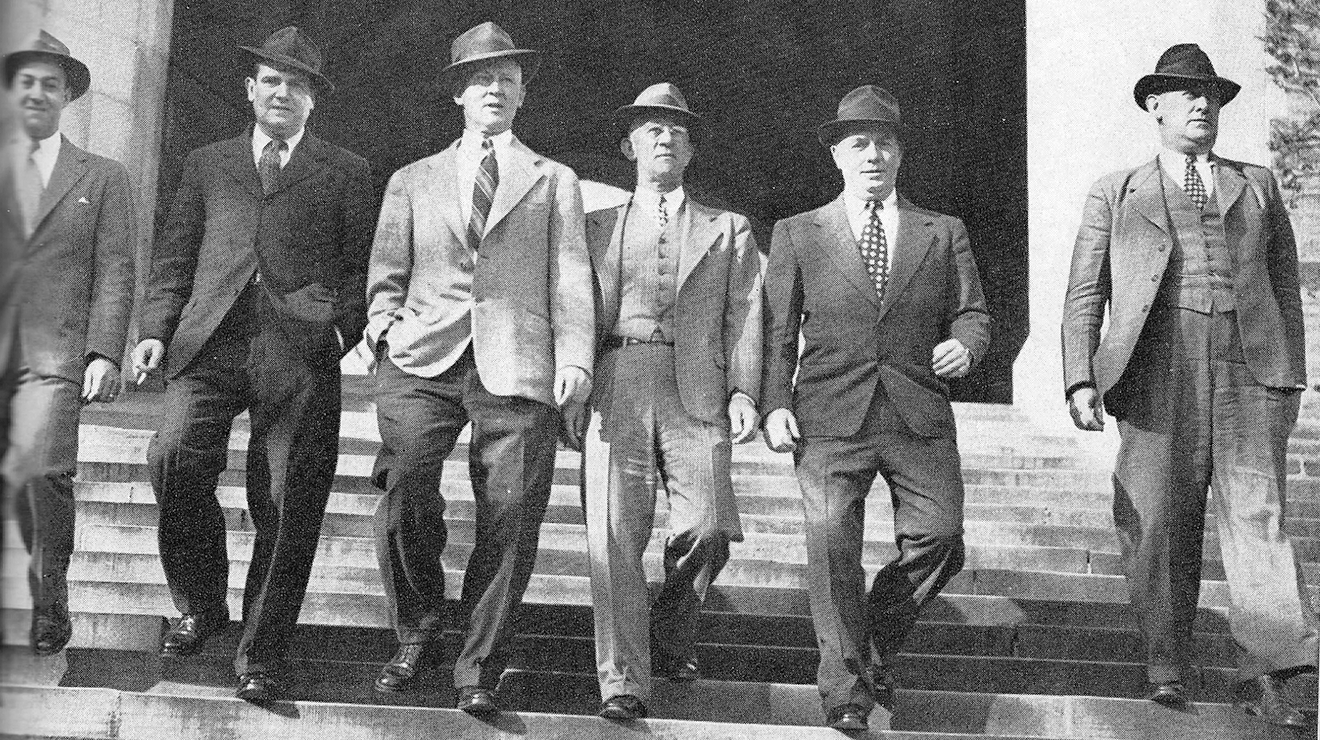 Six men in suits and hats walking down a wide staircase