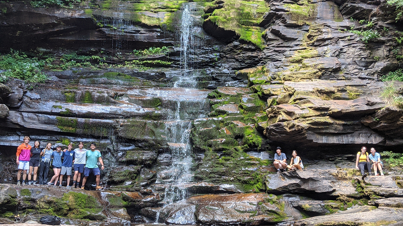 Hiking group poses alongside a waterfall, standing on rock ledges
