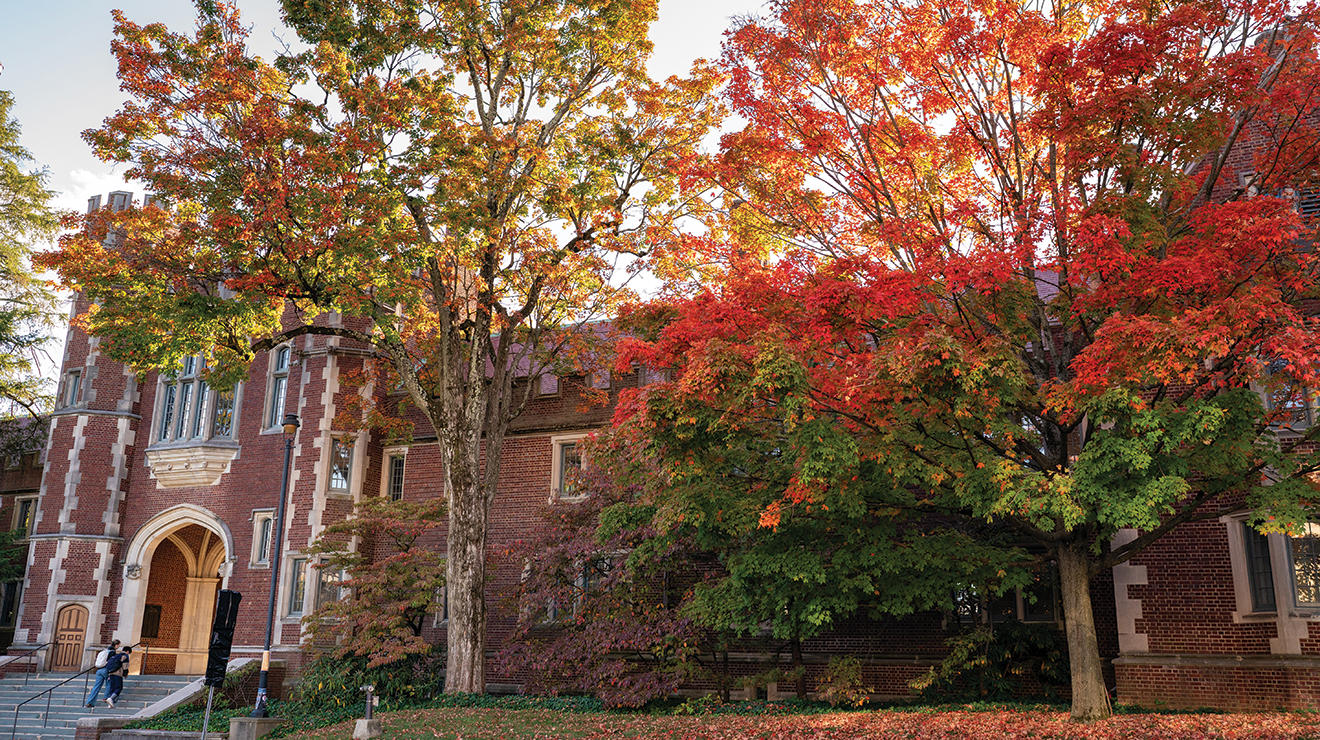 Trees turn red, yellow, and orange in front of a Gothic brick building.