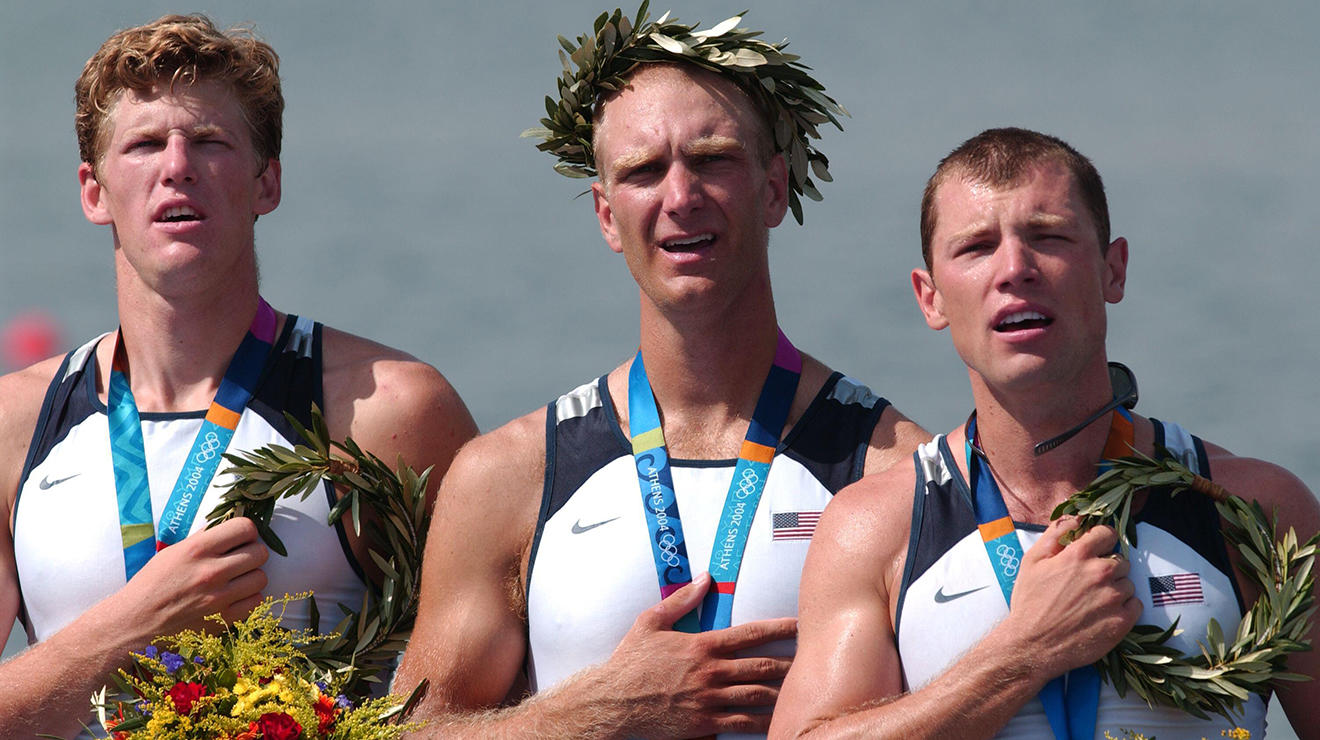 Three men hold hands over their hearts during an Olympic medal ceremony.