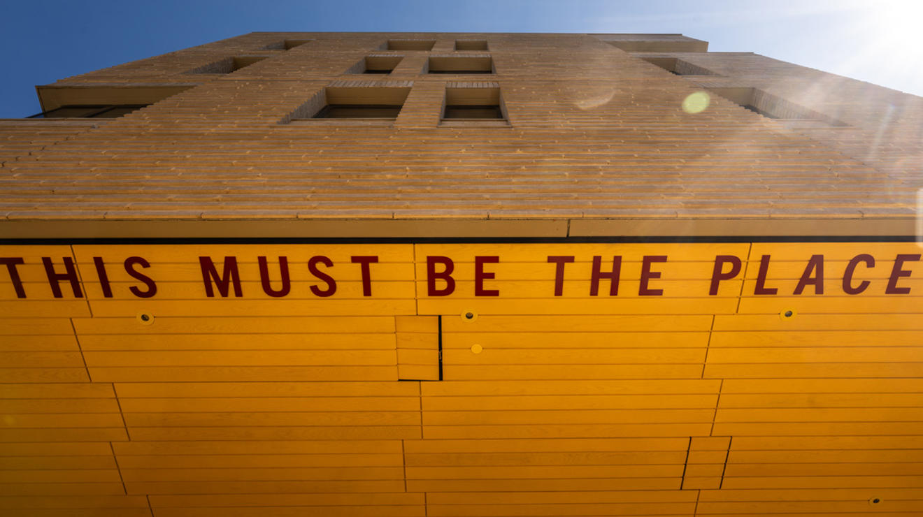 Architectural detail of Yeh College showing the underside of an overhang decorated with bright yellow tiles and the words This Must Be the Place in red letters written on the ceiling
