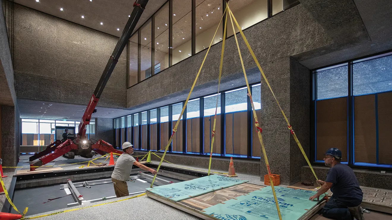 Men lift a Roman floor mosaic into a spot on the floor using a system of ropes and pulleys.