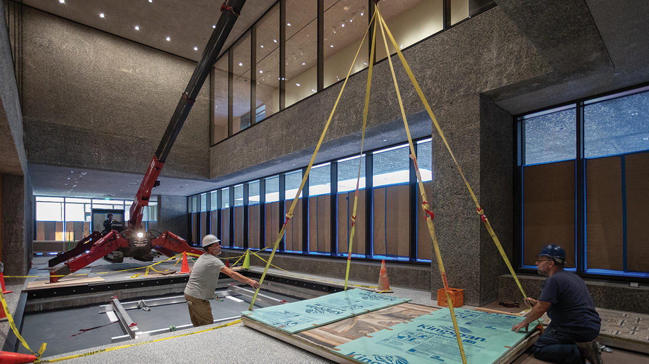 Men lift a Roman floor mosaic into a spot on the floor using a system of ropes and pulleys.