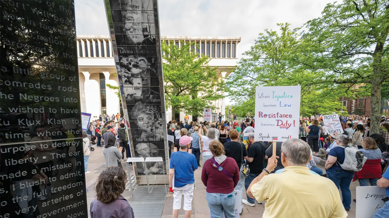 Marchers hold signs at a rally for May Day at the Fountain of Freedom
