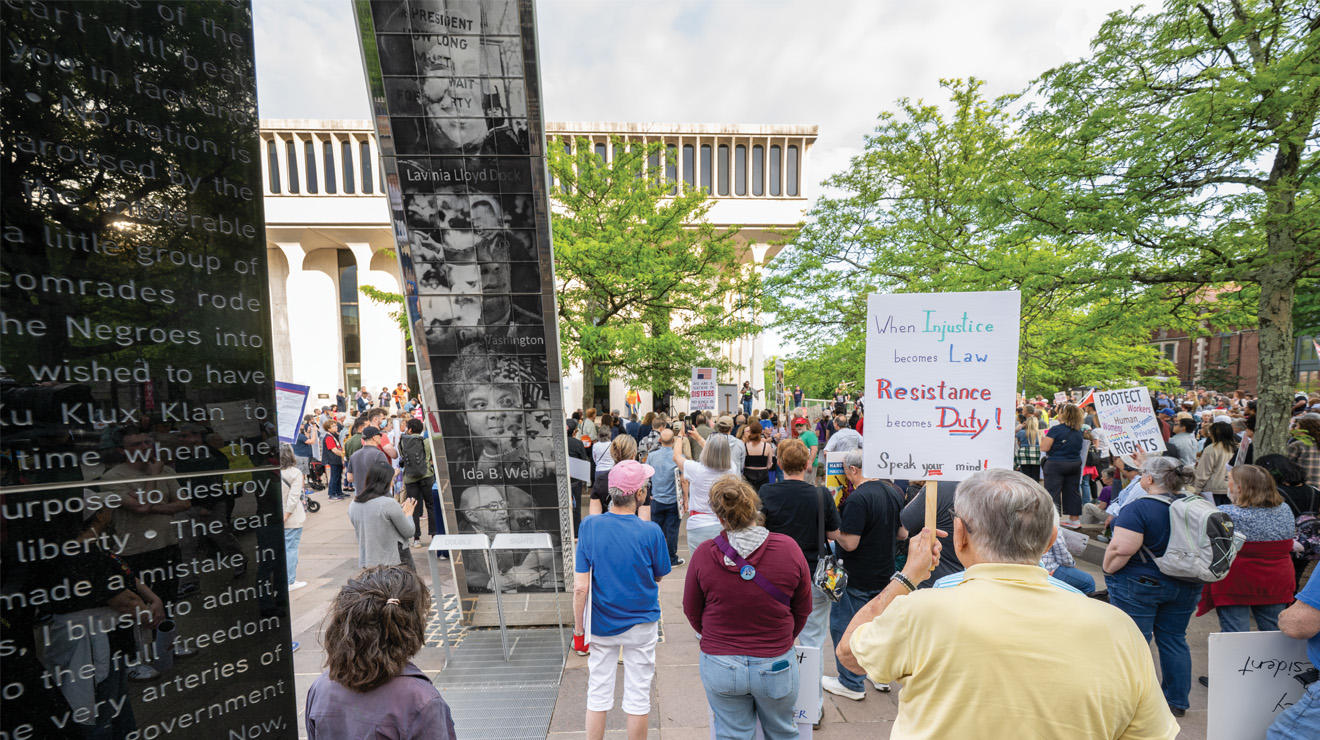 Marchers hold signs at a rally for May Day at the Fountain of Freedom