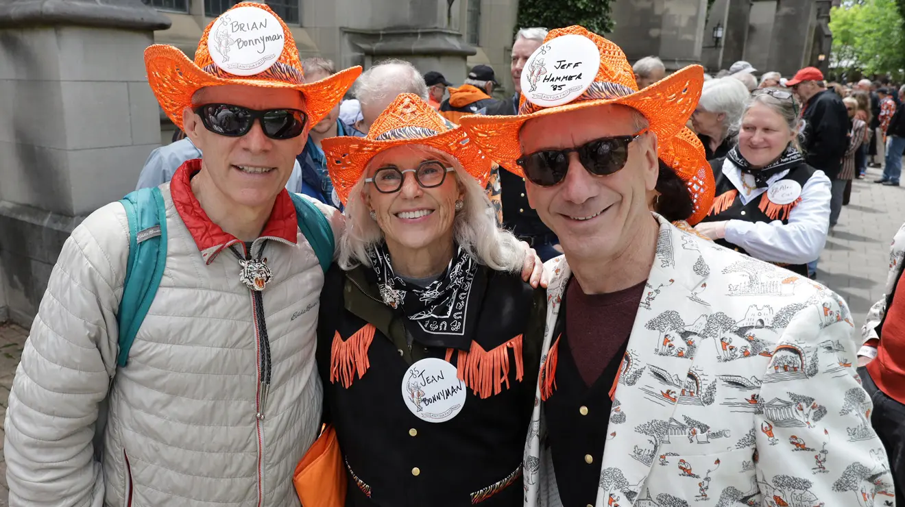 Three people wearing orange cowboy hats smile for the camera.