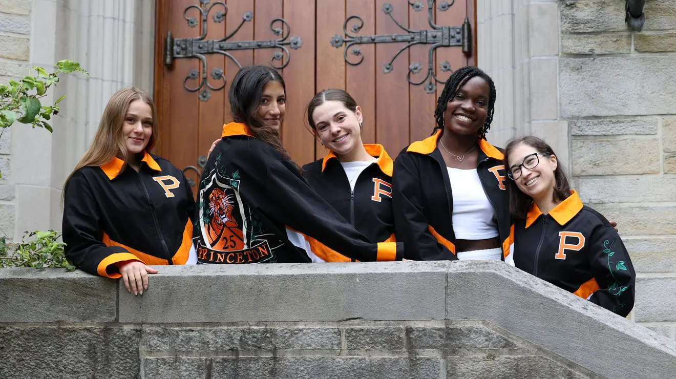 Five women from the Class of 2025 wear their black and orange class jacket and smile toward the camera.