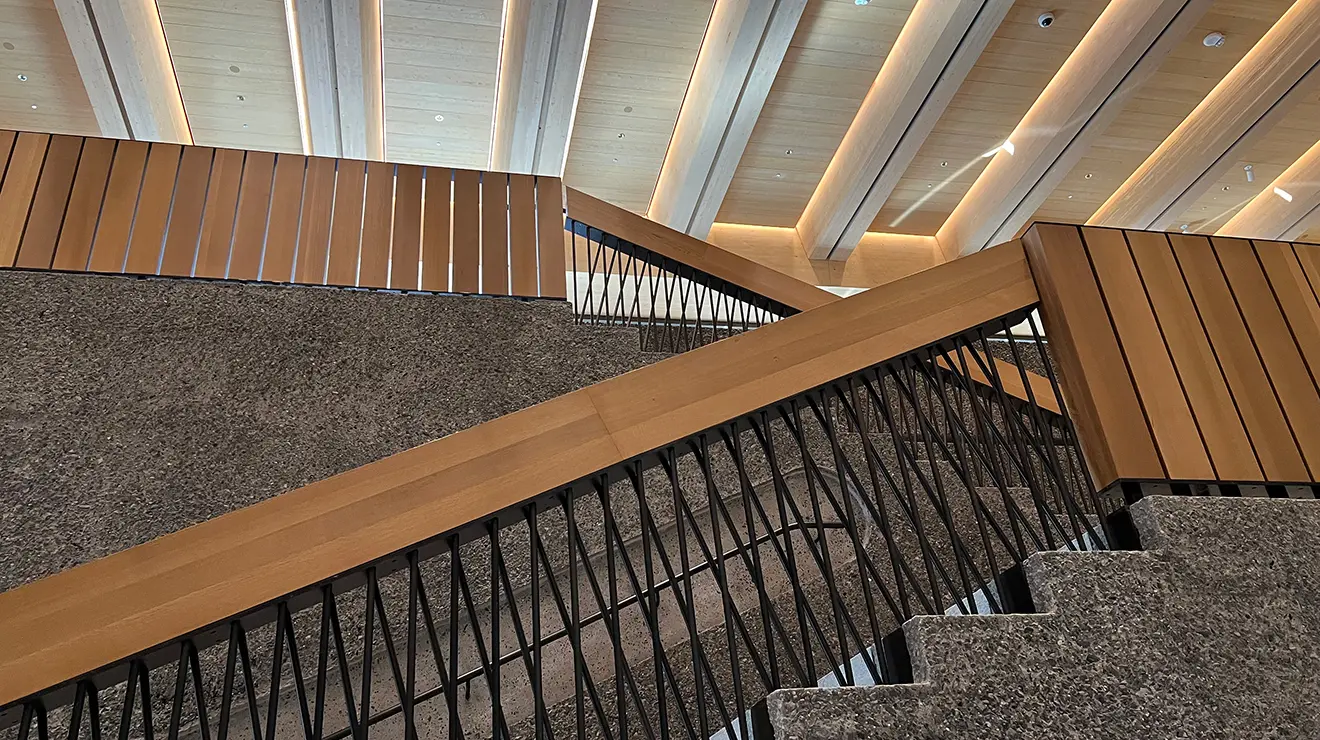 ARTMUSEUM_Main_stairs.jpg View up a staircase with wood railings, black supports, and gray concrete walls. The ceiling above is light wood.