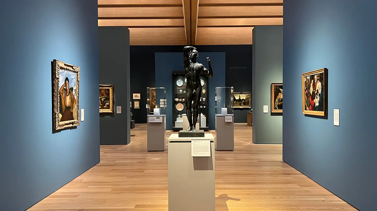 ARTMUSEUM_Rodin_room.jpg A gallery with blue walls and pale wood floors and ceiling; a black stone statue stands in the center.