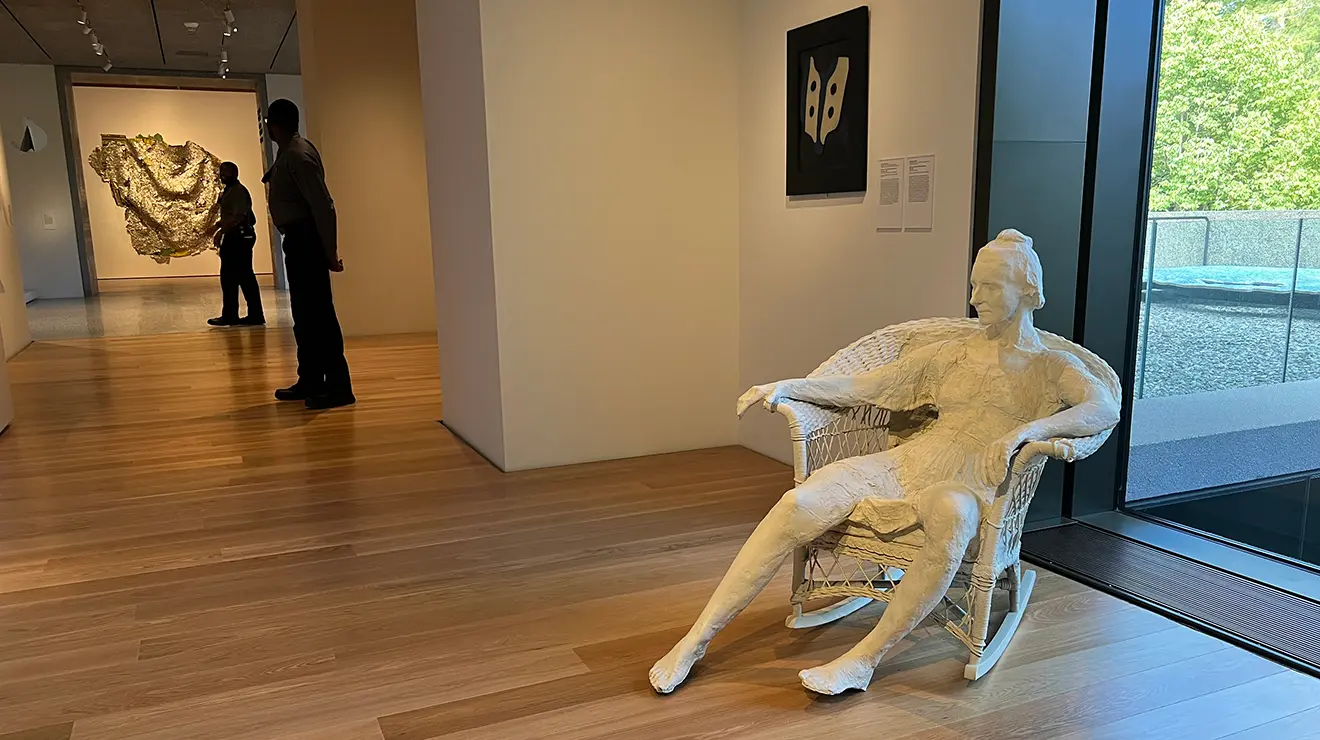 ARTMUSEUM_Woman_in_chair.jpg A white sculpture of a woman sitting in a rocking chair, next to a window.