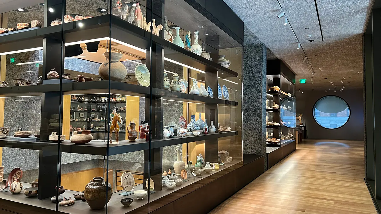 Artwalk2.jpg Art and artifacts fill glass cases along a second-story hallway; a round window is at the hallway's end.