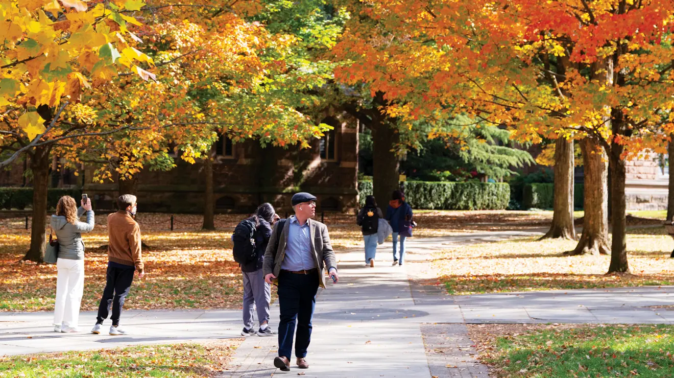 Man walk across campus with fall trees beautiful colors