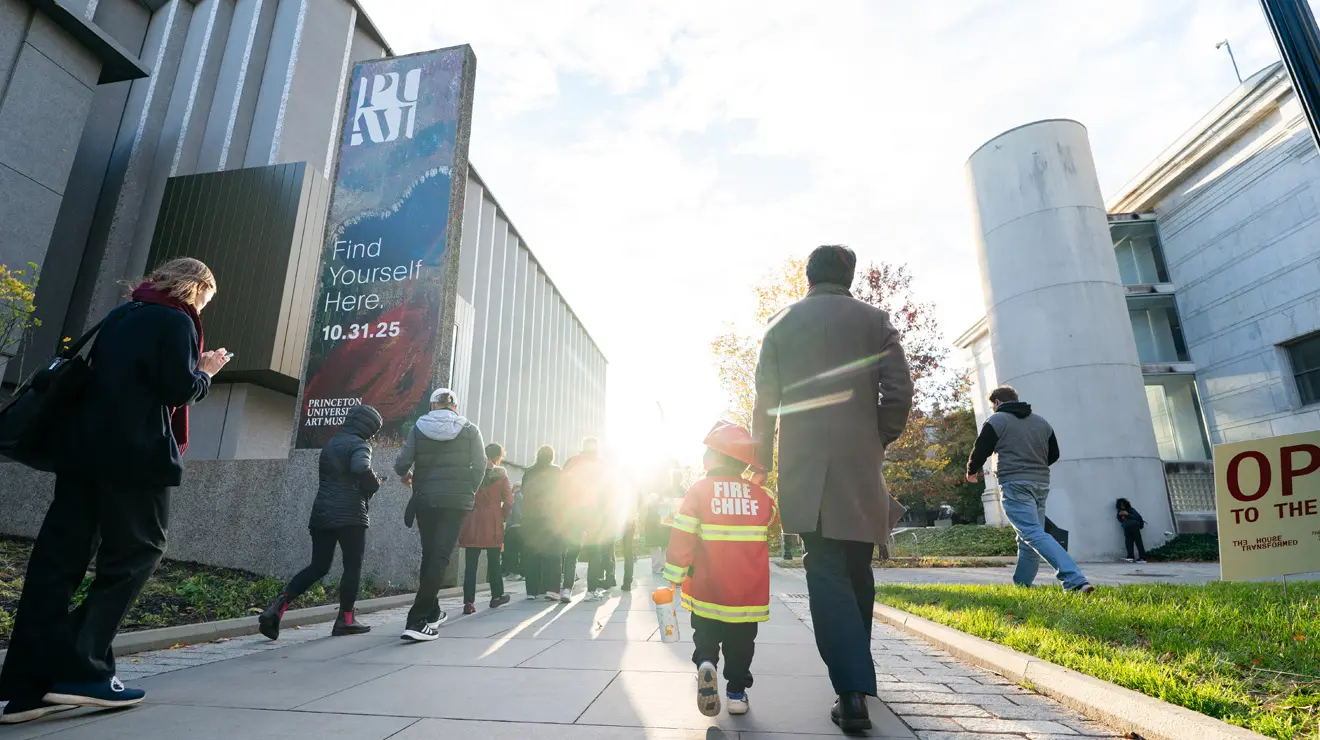 PAUM OPENING_Fire Chief.jpg A small child dressed as a firefighter holds an adult's hand while walking toward the entrance of the Princeton University Art Museum.