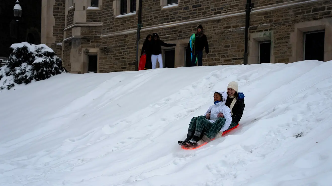 Two people ride a sled together down a snowy hill by Blair Arch.
