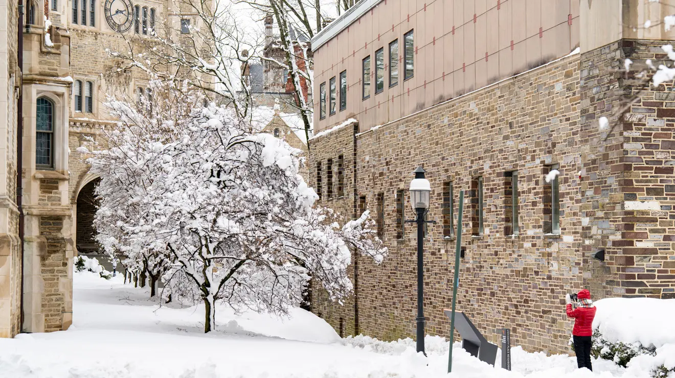 Student is red coat takes a photo of the snow covered campus after blizzard