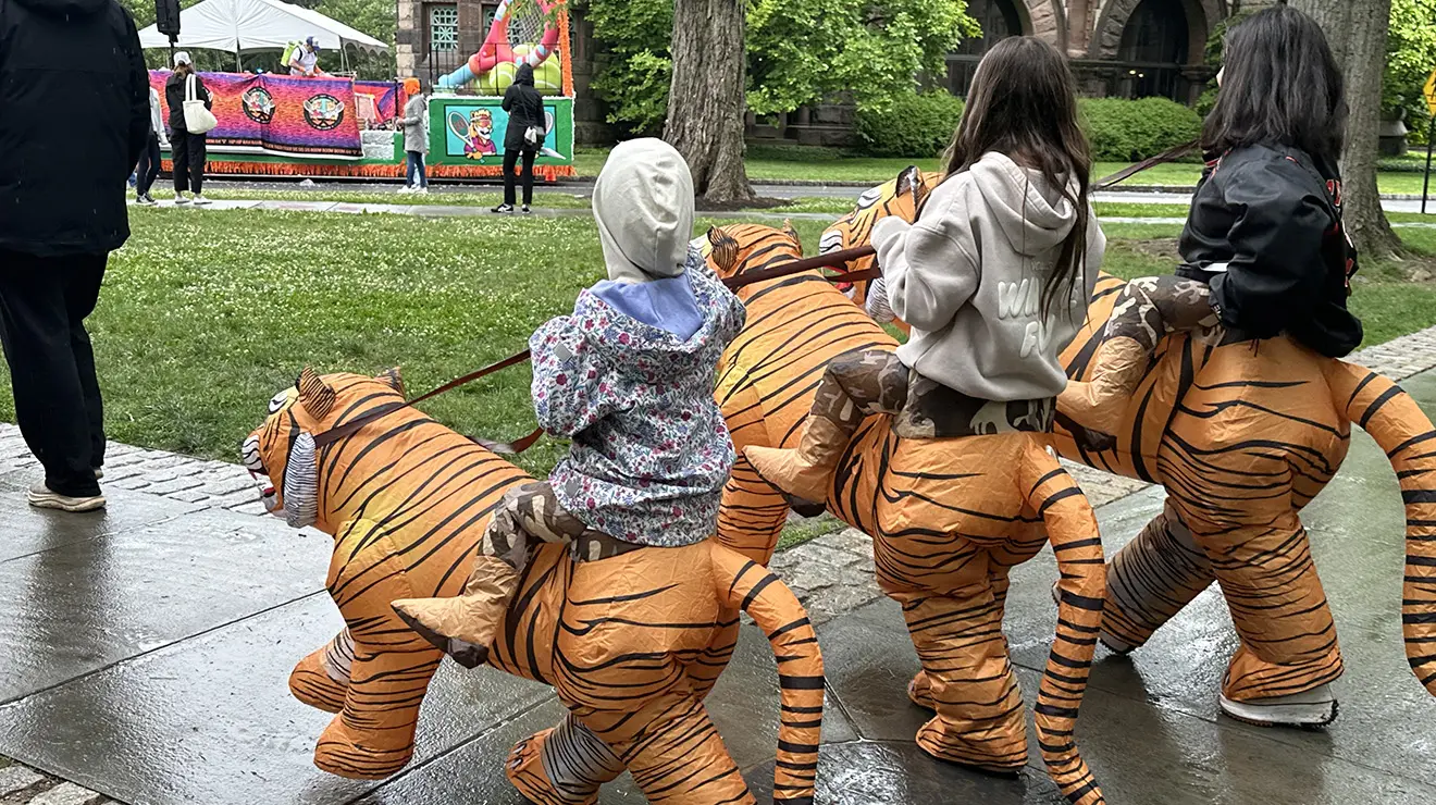 Three children walk in inflatable costumes that look like they're riding on tigers.