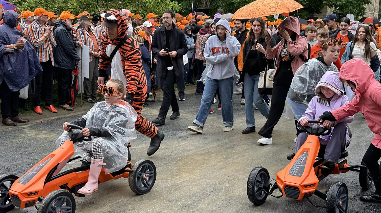 Marching in the P-rade are two kids driving orange go-karts.