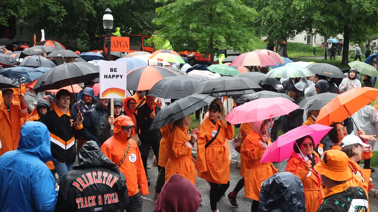 A crowd of people wearing orange and carrying umbrellas; someone holds up a sign with a rainbow and the words "be happy."
