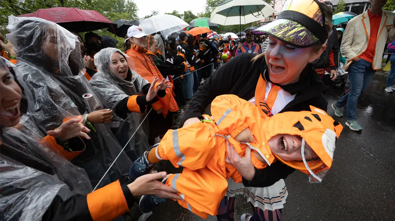 A parent holds a happy but unruly toddler wearing an orange raincoat.