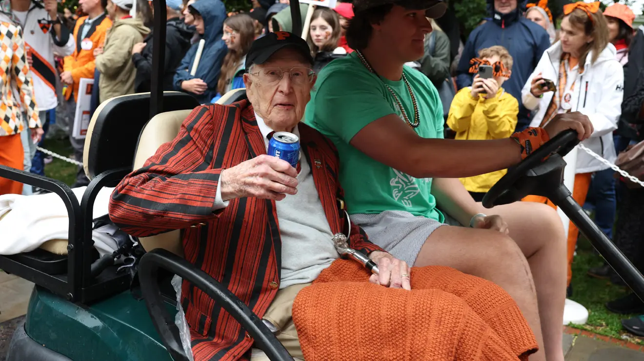 A man holds a beer as he rides in a golf cart.