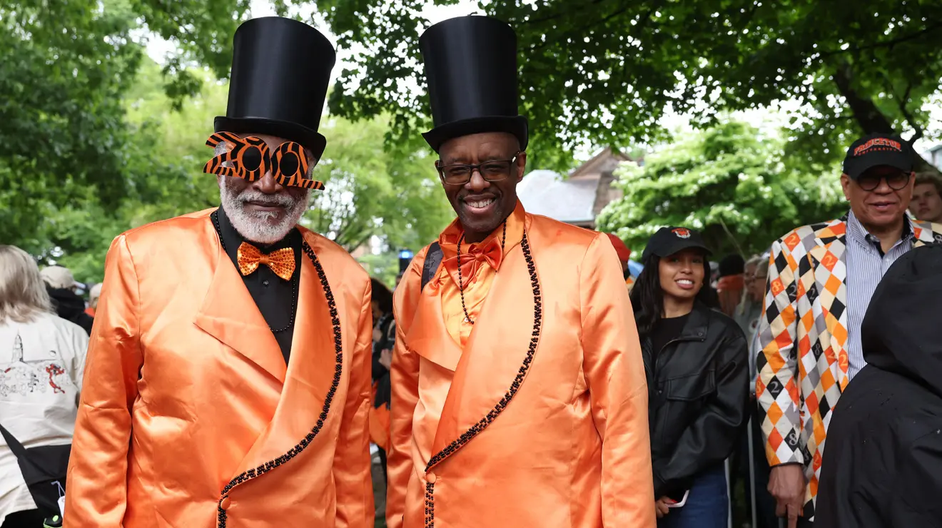 Two men wear satiny orange suits and black top hats.