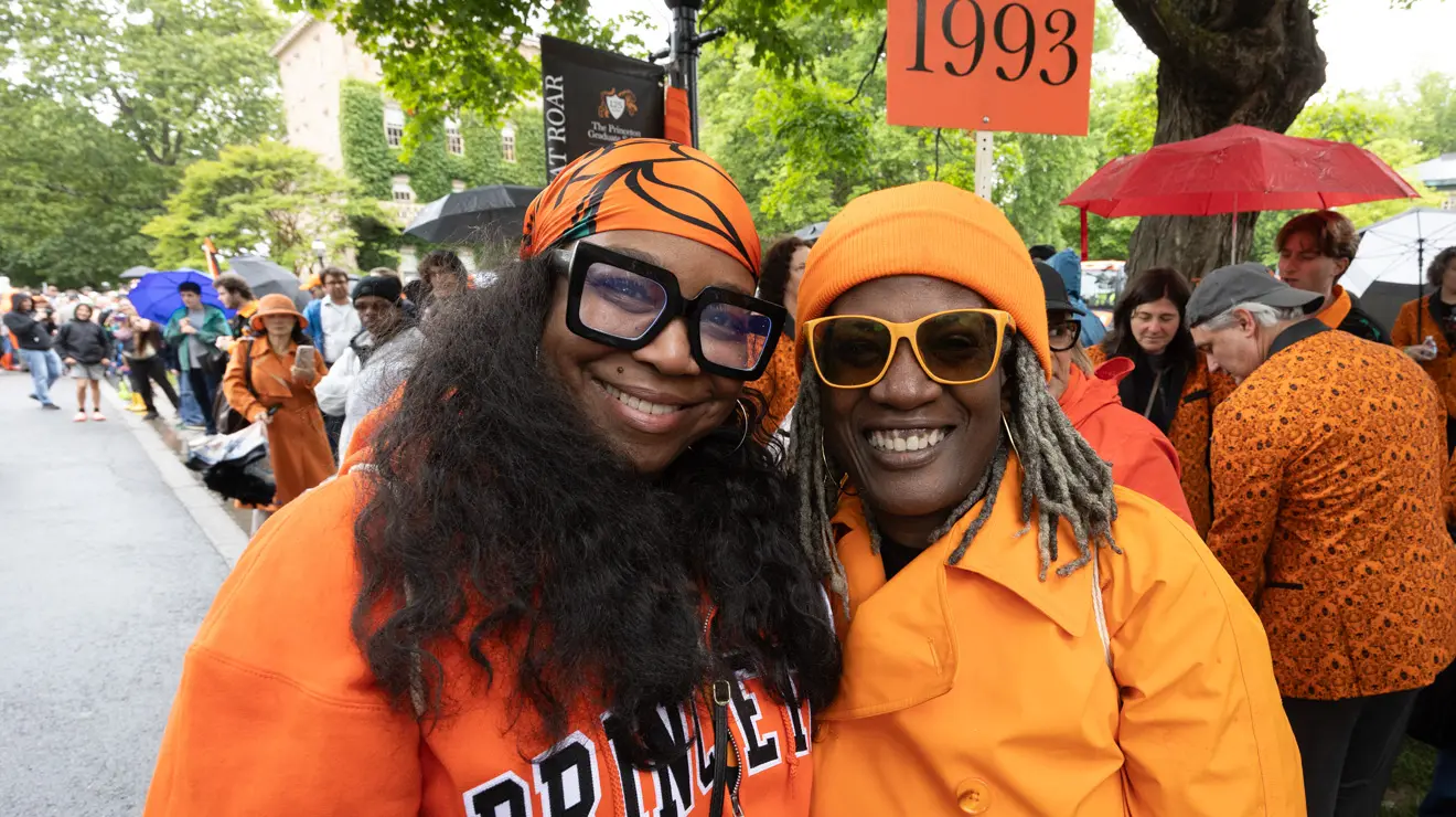 Two women wear orange clothes in front of a sign reading 1993.