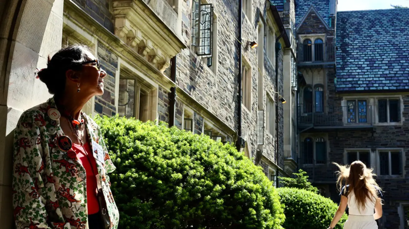 A woman looks up from the doorway of a Gothic Princeton building; another woman runs in the background.