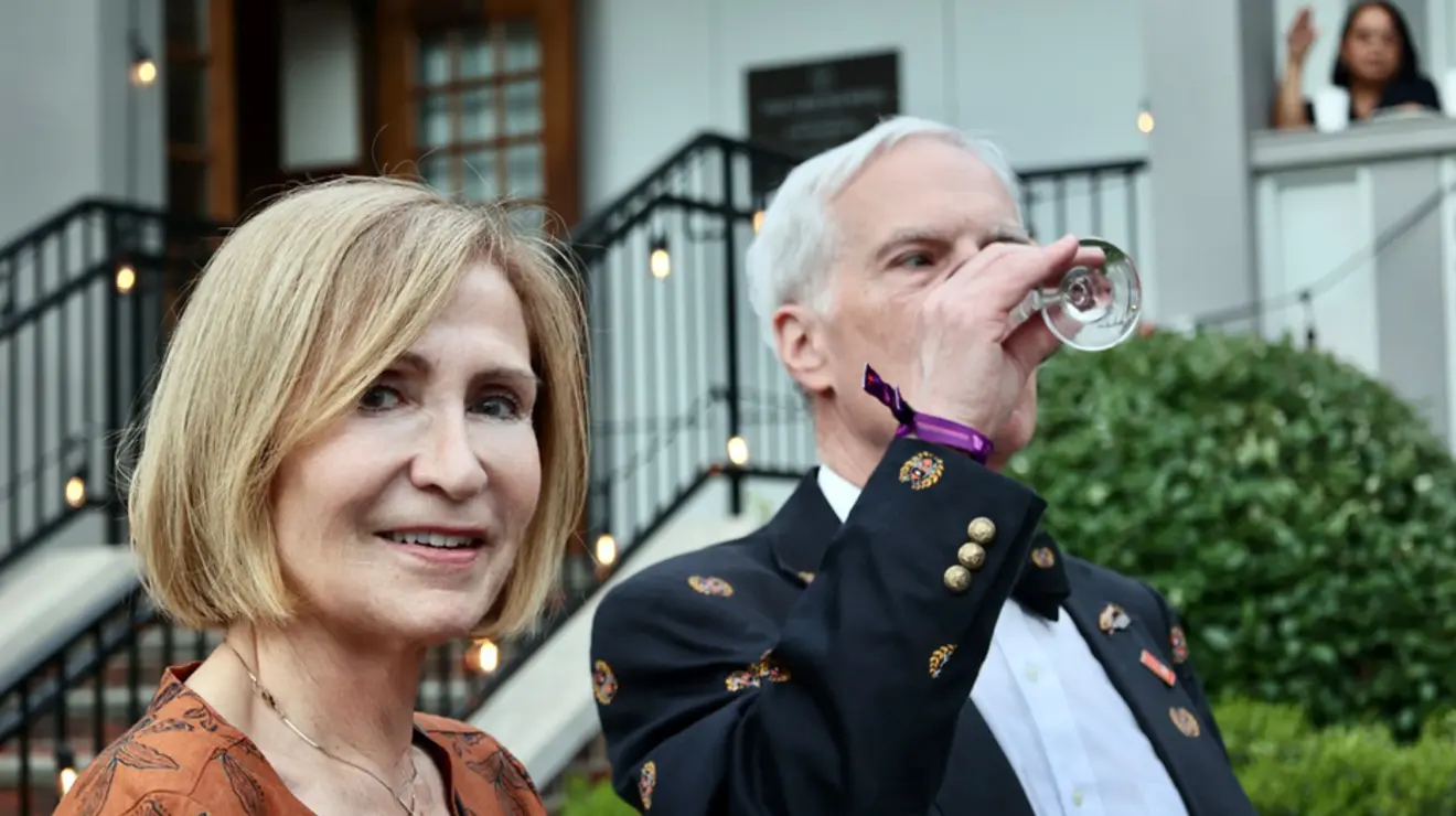 A man drinks a glass of wine; a woman smiles for the camera.