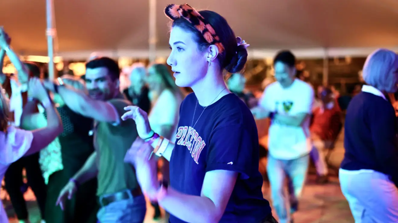 A woman dances in a tent while wearing a tiger ears headband. 