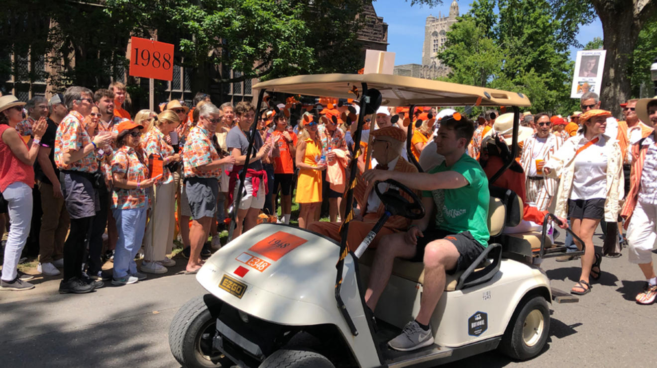 A student drives a member of the Old Guard in a golf cart.