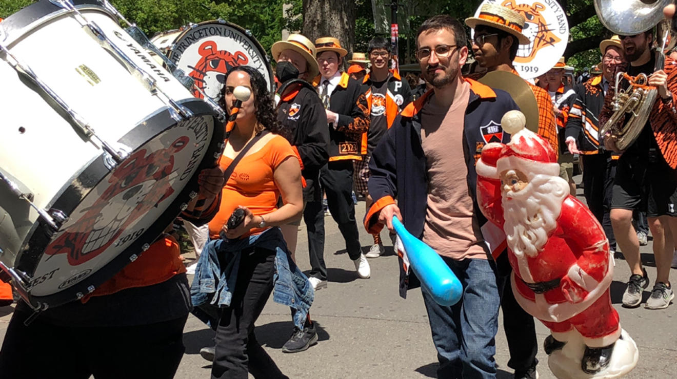 Band members march in the P-rade; one holds a baseball bat and a plastic Santa Clause.