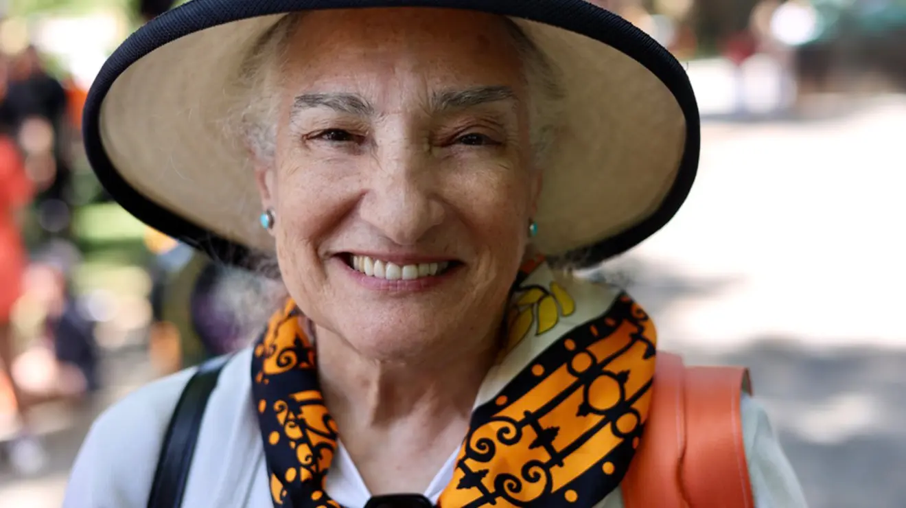 A woman in a hat and orange-and-black scarf smiles for the camera.