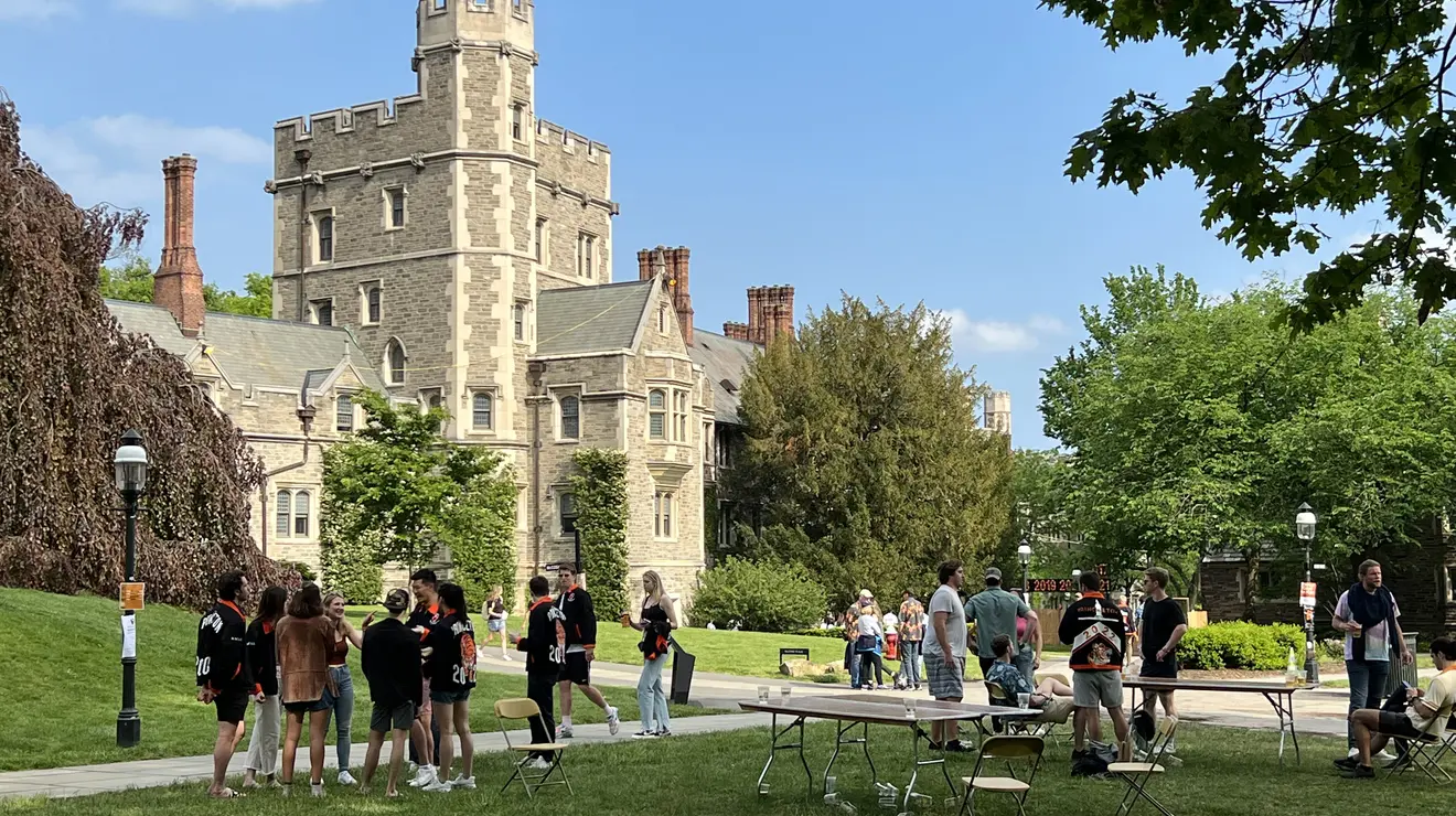 Students socialize by tables in a courtyard, with a stone Gothic building in the background..