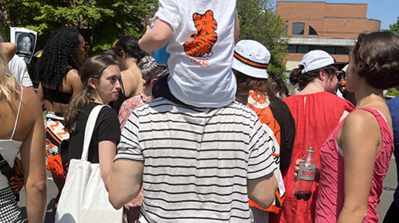CubOnShoulders_liz.jpg A little girl wearing a tiger shirt sits on a man's shoulders, both facing away from the camera.