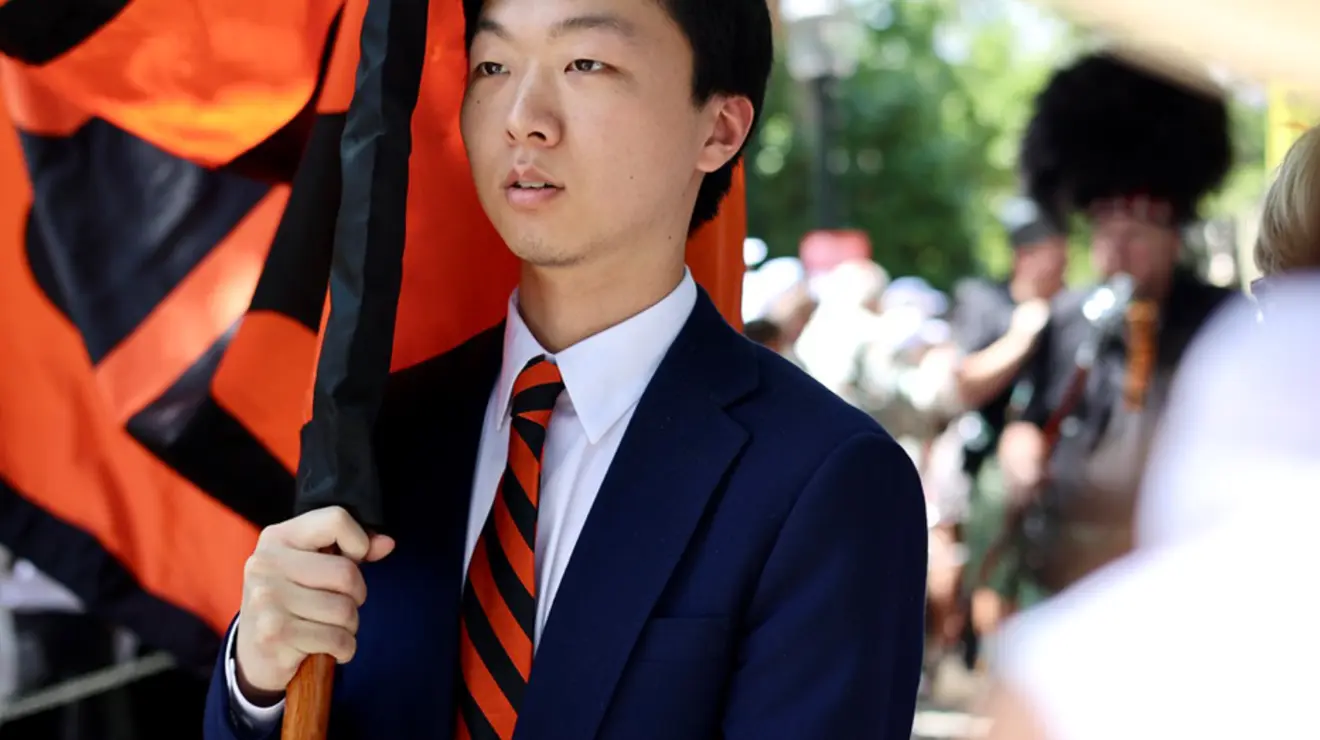 A young man in an orange-and-black striped tie holds one side of a banner.