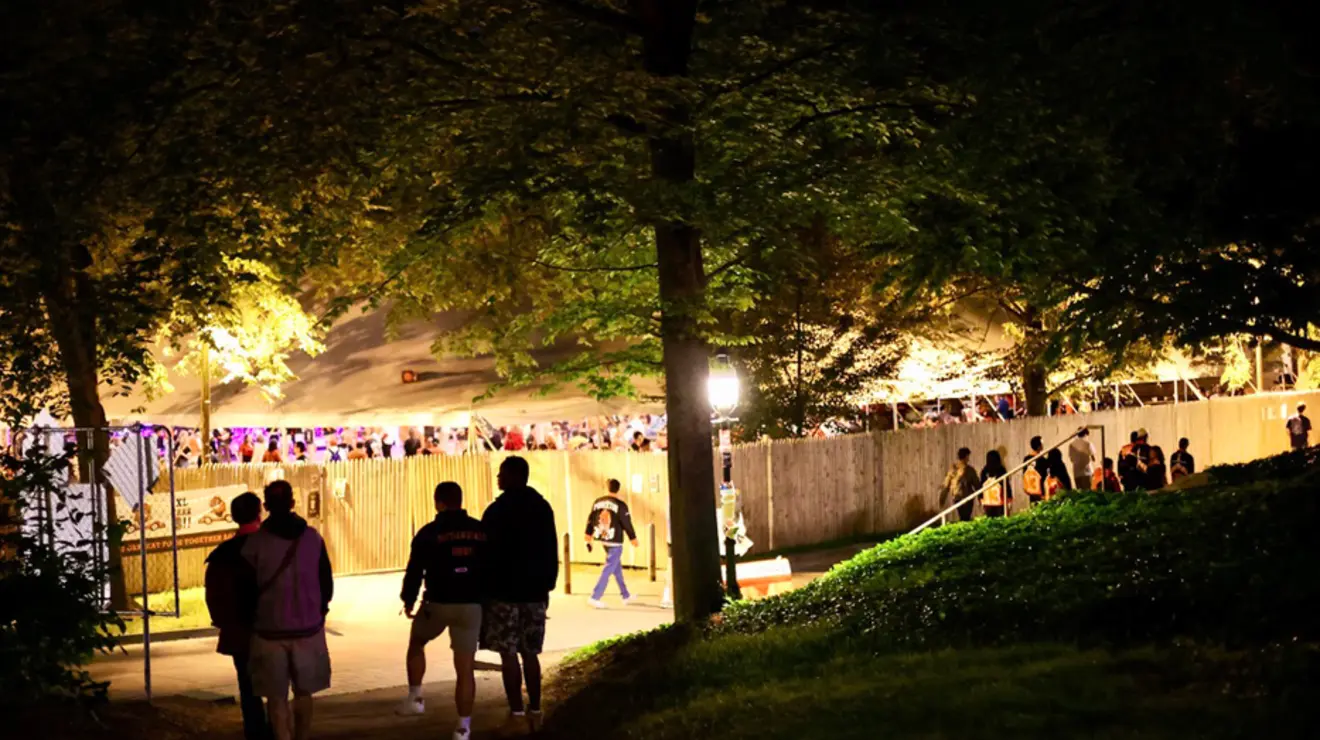 People walk in the dark toward a party behind a wooden fence.