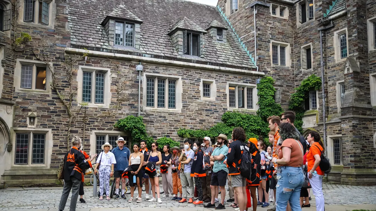 People stand around listening to a speaker in a stone building courtyard.