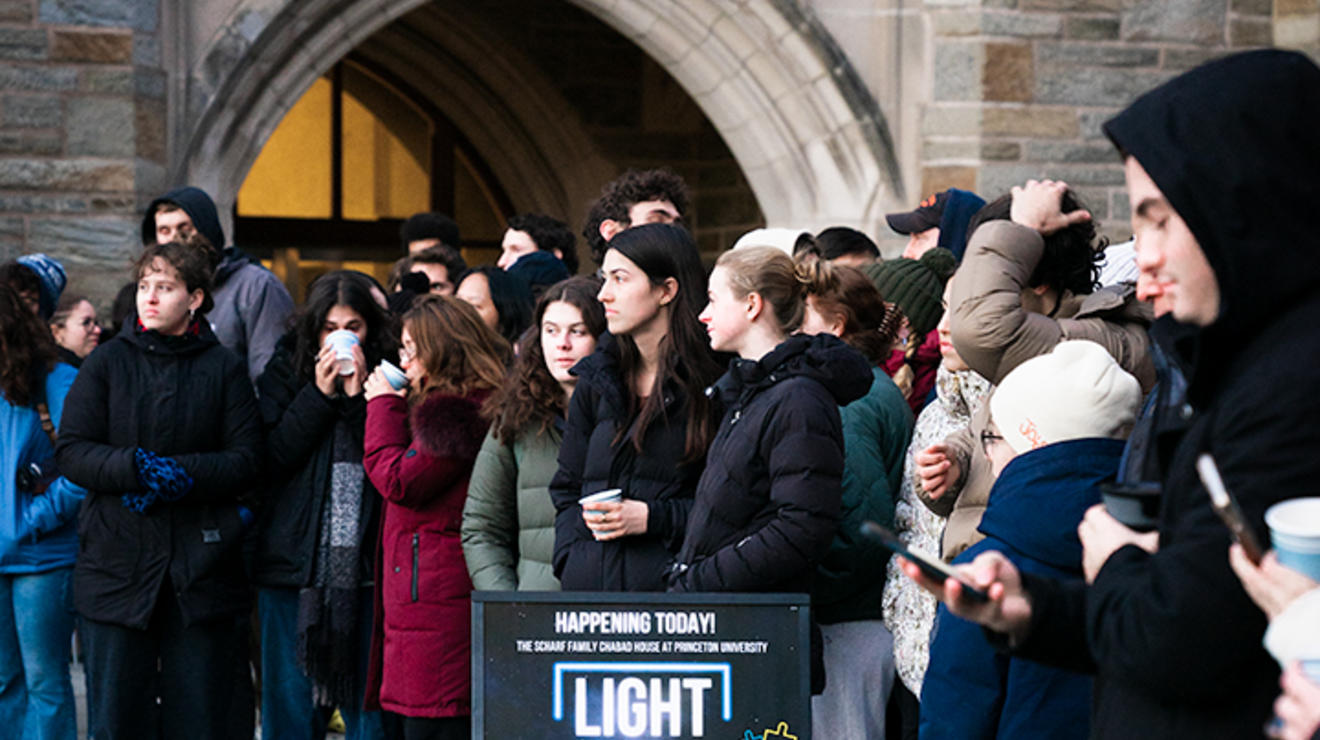 Students gather behind a small sign for the event reading "Light Up Princeton"