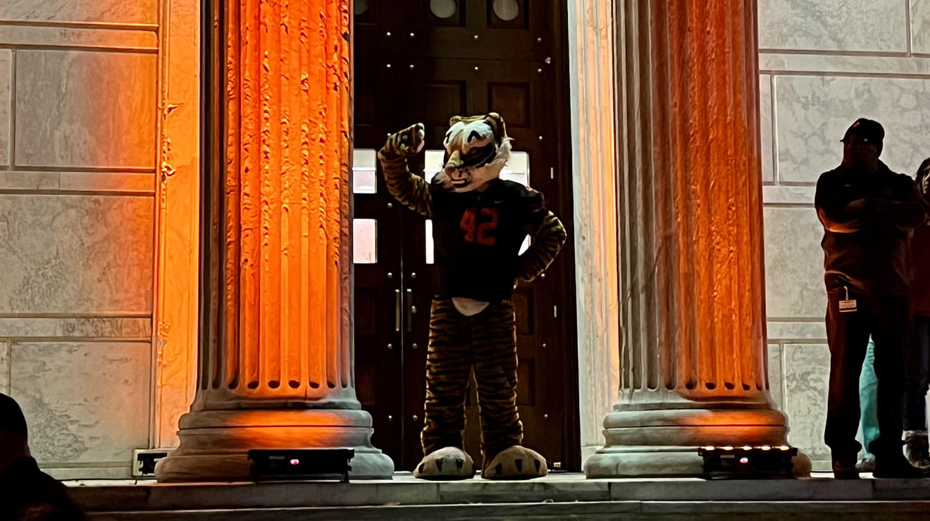 The Princeton tiger mascot stands between two columns lit up with orange lights.