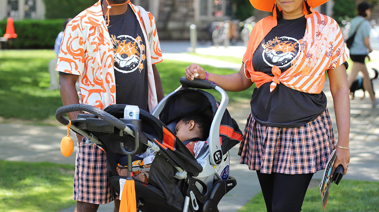 Two people wearing orange hats next to a sleeping baby in a stroller.