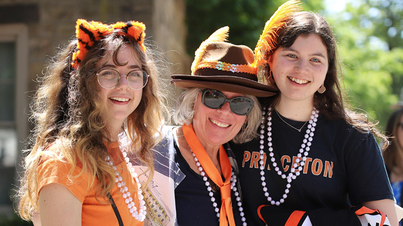 Three women wearing black and orange clothes and long pearl necklaces.