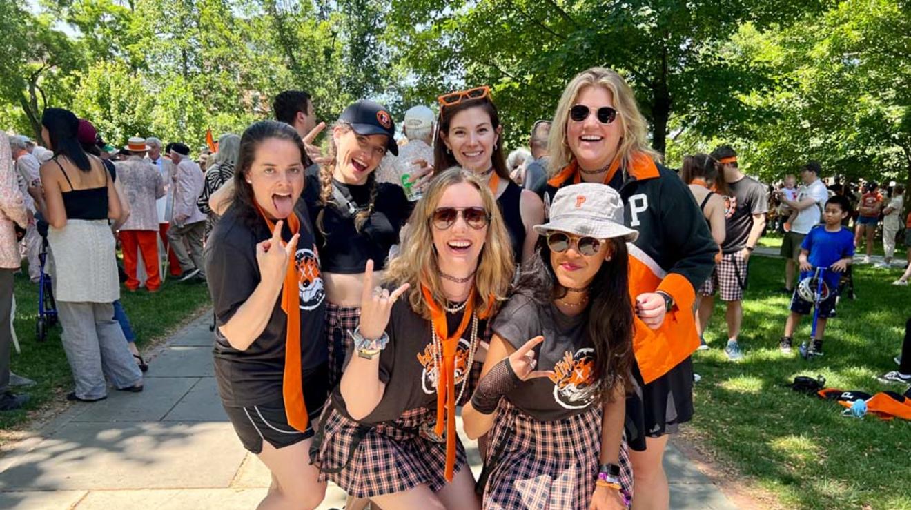 Six women wearing orange ties and black-and-orange gingham skirts.