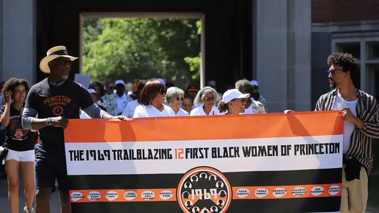 PRADE23_Allison-26.jpg Two guys carry a banner reading "The 1969 Trailblazing 12 First Black Women of Princeton."