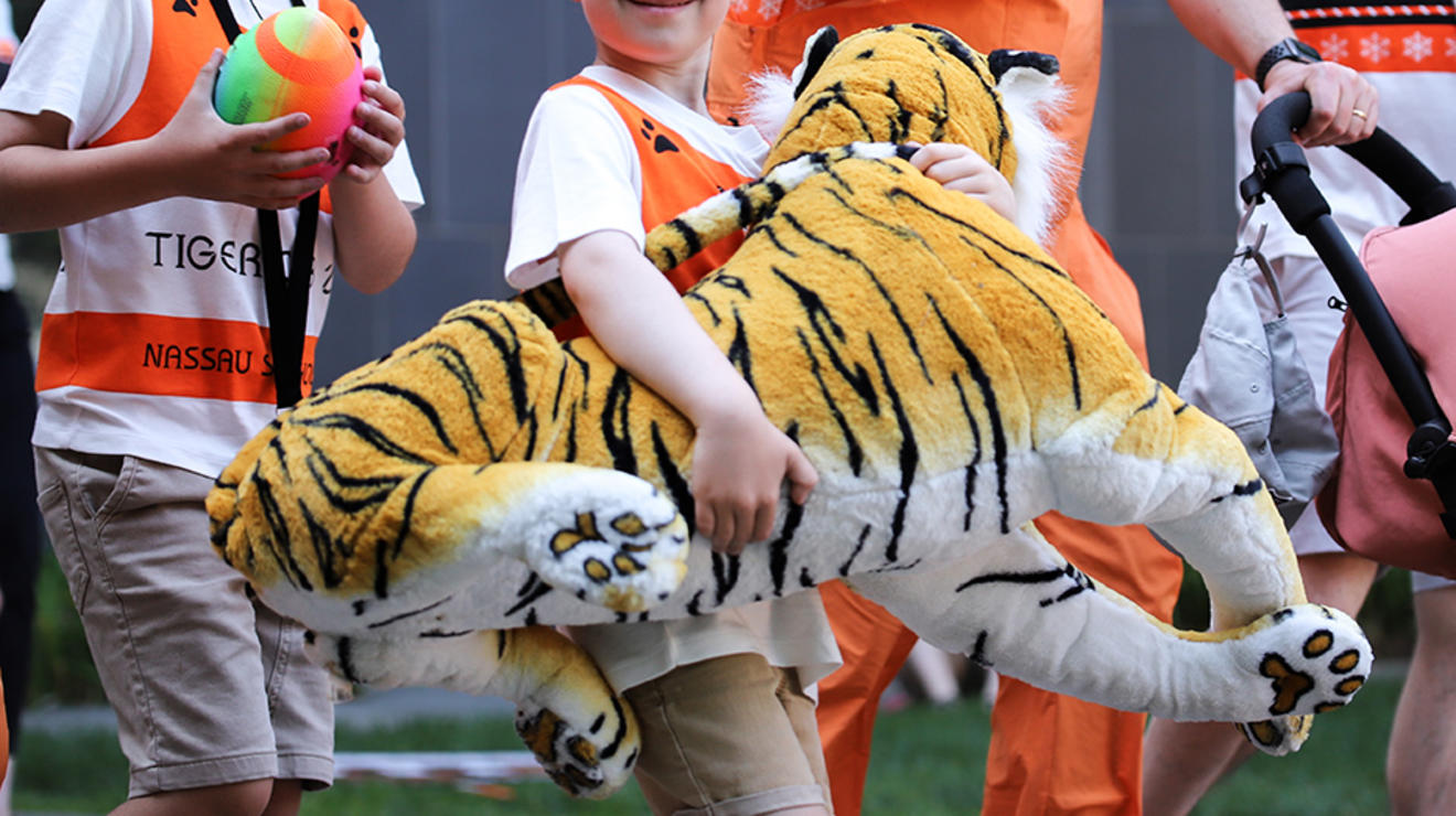 A kid carries a big plush tiger.